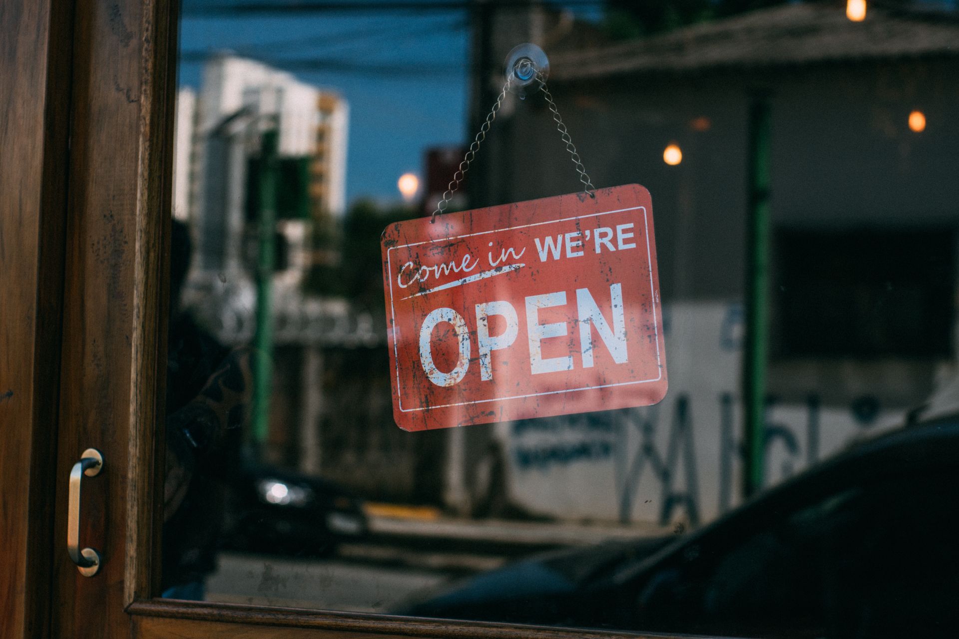 Red signage hanging in a door with "Come in, We're Open".