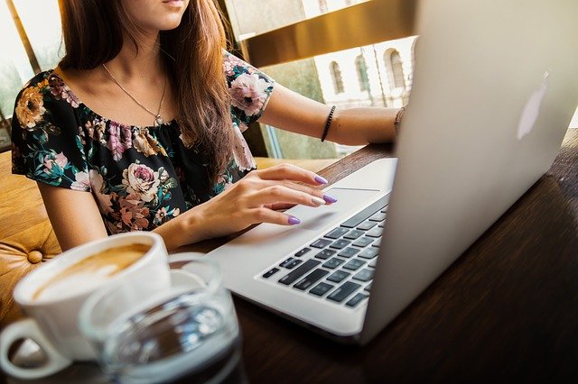 Female sitting at desk with laptop and cup of coffee.